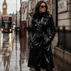 Woman in a black coat standing on a rain-soaked street with a double-decker bus and British flag in the background.