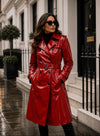 Woman wearing a red trench coat standing on a wet street with a building in the background.